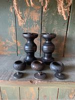 Full lot view with two candle sticks and three lidded boxes on rustic wooden surface with green distressed wood background