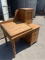 Front-right angled view showing slant top, Sheraton turned leg, three drawers, and cabinet with hinged door above.