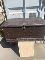 Front view of antique seafarers trunk showing dark brown paint, metal latch, and base condition.