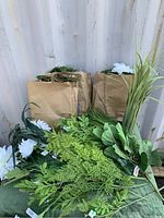 Various artificial green plants and three paper bags filled with moss, showing different types of green foliage.
