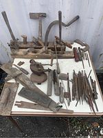 Overall display of antique tools showing wooden hand planes, files, sickle, and mini vise on tabletop.