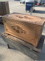 Photo of the front and top of the carved wooden blanket chest showing detailed geometric and swirl carvings with floral borders.