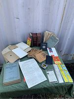 Wide shot of all papers, books, booklets, envelopes, and ephemera spread on a dark green cloth with a container behind them.