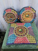 Lot shows two round cushions and one square cushion stacked on a textile storage hassock, all featuring embroidered colorful patchwork with elephant motifs and tassel trim.