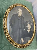 Front view of the antique framed photo print showing the man and woman in early 20th century attire with carved ornate oval frame.