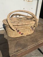 Side view of oval hand woven Malawi rush basket with fitted lid and looped handles. Shows color pattern and weaving details.