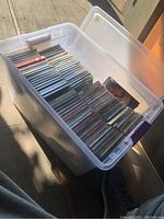 Photo of the transparent plastic tub filled with a large quantity of Compact Discs organized vertically in jewel cases.