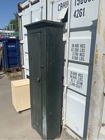 Full view of tall, narrow chimney cabinet with rustic dark green paint and single door.