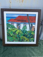 Framed oil painting showing tropical scene with white house, red roof, and large green leaves