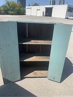 Open cupboard showing interior with three shelves, wood surfaces worn and aged.