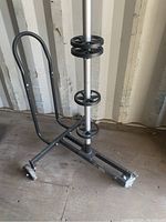 Side angled view of the standing tire storage rack showing the vertical pole with three circular tire holders, frame base with two wheels, and handle.