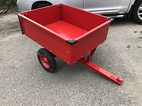 Red steel tilting garden cart viewed from a front-side angle on asphalt with car in background