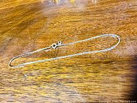 Photo of thin gold bracelet laid flat on wooden surface showing length and chain detail.
