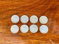 Top view of eight 1967 Canadian silver quarters arranged on a wooden surface, showing the leaping cougar side.