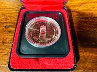 Front view of the 1977 Canadian Silver Dollar commemorative coin featuring the Throne of the Senate design in protective capsule and red velvet clamshell case.