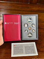 Photo showing the black leather Royal Canadian Mint case opened to reveal the proof coin set with 7 coins including a large silver dollar and informational card beneath