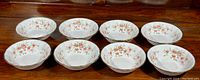 Eight matching white porcelain salad/pasta bowls with floral Victoriana Rose pattern and gold gilt edging arranged in a row on a wooden surface.