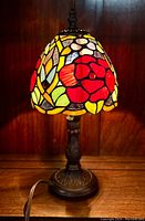 Full view of the Tiffany style table lamp turned on, showing stained glass floral shade and metal base