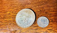Front view of the 1968 Mexico Olympics coin and the 1839 British six pence coin side by side on a wooden surface.