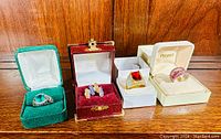 Four vintage sterling silver rings in original boxes displayed on wooden surface.