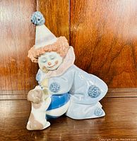 Front view of the Lladro Pierrot clown figurine showing clown face, curly wig, hat, suit with pompoms, blue and white ball, and puppy.