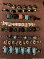 Full view of 8 link bracelets laid on brown fabric surface showing various colors and styles