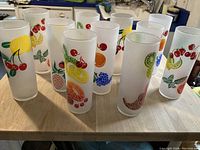 Set of 12 tall frosted glass highball glasses with colorful fruit designs arranged on a wooden surface.