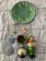 Overview of lot with Majolica plate on top, glassware, figurine, and metal creamer pitcher on blue quilted background