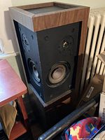 Speaker with wood veneer cabinet and black speaker panel showing woofer, midrange, and tweeter drivers