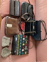 Eight assorted purses shown together on a pinkish couch including leather, patent leather, fabric, and beaded bags.