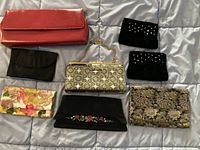 View of all 8 clutches and jewelry cases laid out on a light background, showing variety in colors and materials including red leather, black fabric, floral patterns, and metallic silver tones.