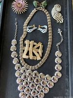 Photo showing entire jewelry lot on black tray including bib necklace, geometric necklace, floral brooch, swirl brooch, white swirl earrings, green beaded earrings, and pins.