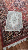 Large red, blue, and white area rug with intricate pattern, small cream floral rug on top