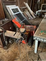 Photo showing orange and white ARIENS snowblower in a cluttered barn space, front left angle with visible wires and controls.