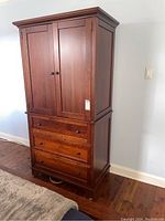 Front view of the wood armoire showing double cabinet doors on top and three drawers underneath with round metal knobs.
