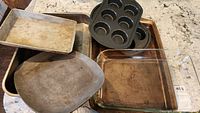 Various metal roasting pans, a glass Pyrex baking dish, and dark metal muffin tins in a group photo showing all items together.