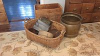 Wide view of all items including a large woven basket filled with small baskets and metal boxes, a brass planter, a vintage wooden box, and a wooden crate in the background.