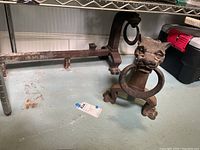 Side view of one brass fireplace dog showing lion head holding ring and base with paw feet.