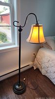 Full view of black metal floor lamp with beige shade lit, showing overall structure and curved arm.