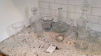 Full view of all glass decanters, vases, and extra toppers arranged on countertop to show lot contents and sizes.