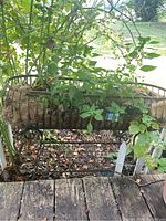 Front and partial side view of metal planter box with natural fiber liner containing growing plants set outdoors on a raised wooden surface with ground visible beneath.