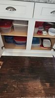 Shelf with multiple plastic food storage containers of various sizes with red, white, and blue lids.