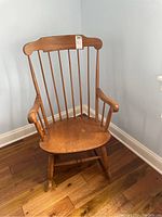 Front view of the wooden rocking chair showing the seat, armrests, and vertical spindle back with scratches.