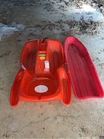 Orange and red plastic sleds placed side by side on the ground.