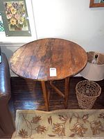 Round wooden folding table viewed from above and side, showing scratches and wear on wooden surface and folding leg structure