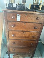 Full view of vintage wooden dresser with five drawers and casters beneath. Each drawer has round wooden knobs and a lock hole, some with stains and general wear.