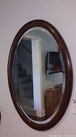 Front view of oval wall mirror showing wood frame and reflection of stairs and furniture.