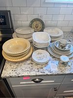 Image showing a large variety of plates including large dinner plates, white square bowls, Libby bowls, small floral plates, and Villeroy & Boch mugs on a granite countertop.