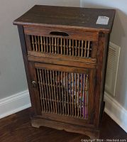 Front angle view of the wood cabinet showing the slatted drawer and lower door with vertical wooden slats and metal door handle. Visible surface scratches on top and sides.