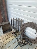 Photo showing the wood crate, bird house, twig wreath, and a small wire basket with driftwood pieces on a wooden porch floor.